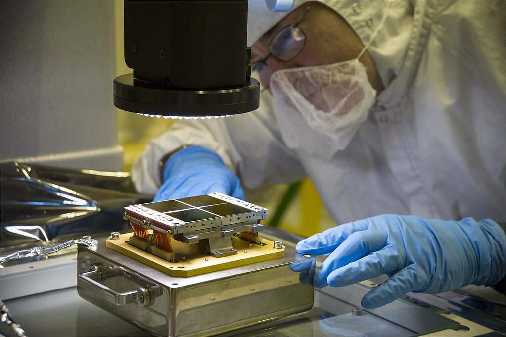 A gowned technician in gloves and face covering carefully aligning a precision instrument under a microscope