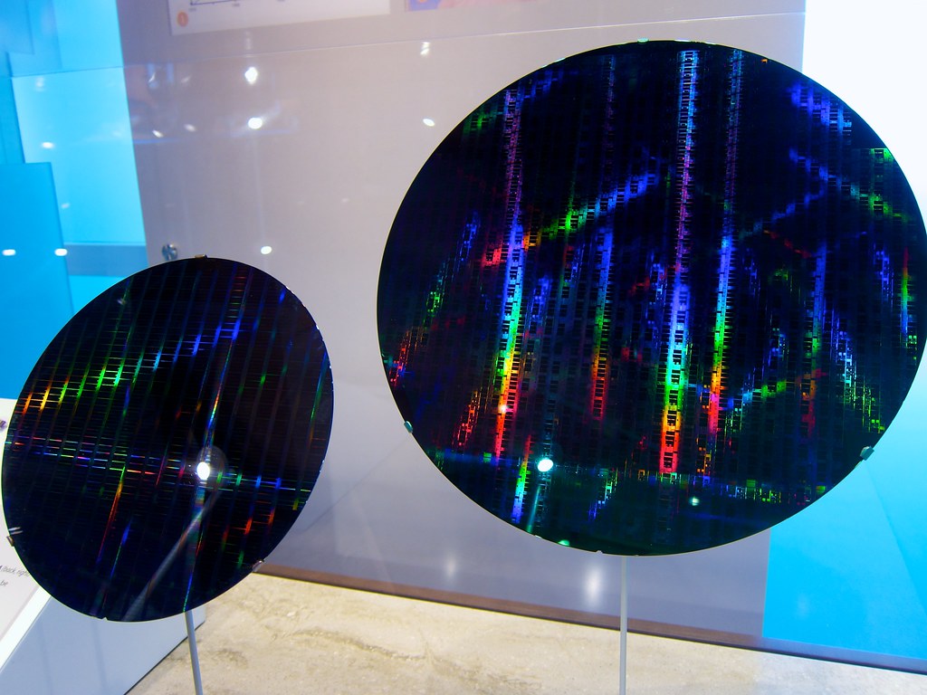 Two finished silicon wafers on display stands, their die grids shimmering in rainbow interference colours